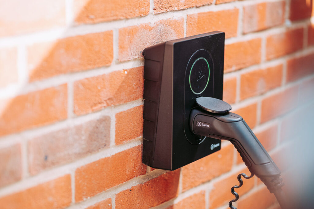 Zwarte Zaptec wallbox met aangesloten stekker tegen bakstenen gevel, oplaadpunt aan huis voor elektrische auto, geschikt voor installatie door LaderThuis.nl monteurs